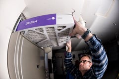 Het manusje van alles vervangt de filter in de hete luchtoven bij een huis stock afbeeldingen Het manusje van alles vervangt de filter in de hete luchtoven bij een huis stock afbeeldingen