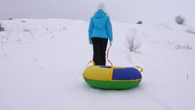 Het meisje beklimt sneeuwberg en trekt slee en een opblaasbare sneeuwbuis rust in het de winterpark voor Kerstmis stock footage Het meisje beklimt sneeuwberg en trekt slee en een opblaasbare sneeuwbuis rust in het de winterpark voor Kerstmis stock footage