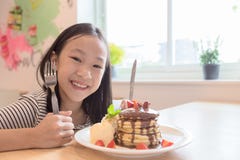 Het meisje glimlacht gelukkig, treft het houden van een mes en een vork voorbereidingen om pannekoeken in restaurants te eten stock afbeelding Het meisje glimlacht gelukkig, treft het houden van een mes en een vork voorbereidingen om pannekoeken in restaurants te eten stock afbeelding