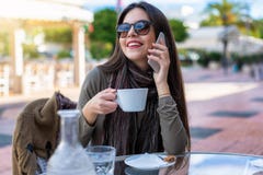 Het meisje zit in openlucht in een koffie en spreekt aan haar mobiele telefoon royalty-vrije stock afbeeldingen Het meisje zit in openlucht in een koffie en spreekt aan haar mobiele telefoon royalty-vrije stock afbeeldingen