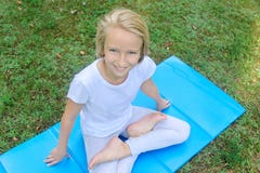 Het mooie blonde preteen meisje in lichte kleding het praktizeren yoga op een mat in het park Gezonde Levensstijl Royalty-vrije Stock Fotografie Het mooie blonde preteen meisje in lichte kleding het praktizeren yoga op een mat in het park Gezonde Levensstijl Royalty-vrije Stock Fotografie