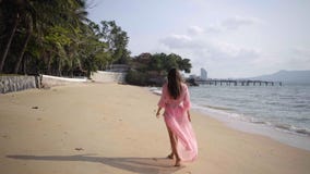 Het mooie wijfje in een lange ontwikkelende roze kleding loopt het lopen rond het spinnen op het strand op de rotsen Close-up 4K stock foto Het mooie wijfje in een lange ontwikkelende roze kleding loopt het lopen rond het spinnen op het strand op de rotsen Close-up 4K stock foto