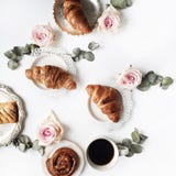 Het ontbijt met roze croissants, nam bloem, bloemblaadjes, uitstekende platen en zwarte koffiesamenstelling toe royalty-vrije stock afbeeldingen Het ontbijt met roze croissants, nam bloem, bloemblaadjes, uitstekende platen en zwarte koffiesamenstelling toe royalty-vrije stock afbeeldingen
