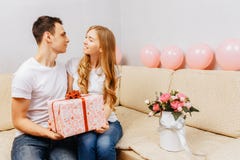 Het paar in liefde, mens geeft een gift, zit de vrouw thuis op de bank, concept de dag van vrouwen stock fotografie Het paar in liefde, mens geeft een gift, zit de vrouw thuis op de bank, concept de dag van vrouwen stock fotografie