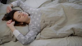 Het portret van jonge donkerbruine vrouw kleedde zich in grijze pyjama die die en in bed liggen slapen met linnen thuis wordt beh stock videobeelden Het portret van jonge donkerbruine vrouw kleedde zich in grijze pyjama die die en in bed liggen slapen met linnen thuis wordt beh stock videobeelden