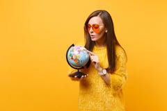 Het portret van nieuwsgierige vrij jonge vrouw in bontsweater, oranje hartglazen die op wereldbol kijken isoleerde op helder royalty-vrije stock fotografie Het portret van nieuwsgierige vrij jonge vrouw in bontsweater, oranje hartglazen die op wereldbol kijken isoleerde op helder royalty-vrije stock fotografie