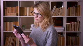 Het profielportret van blondeleraar werken het op middelbare leeftijd met tablet draait aan camera en glimlacht bij de bibliothee stock footage Het profielportret van blondeleraar werken het op middelbare leeftijd met tablet draait aan camera en glimlacht bij de bibliothee stock footage