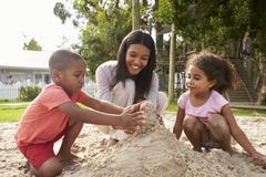 Het Spelen van leraarsat montessori school met Kinderen in Zandkuil royalty-vrije stock foto Het Spelen van leraarsat montessori school met Kinderen in Zandkuil royalty-vrije stock foto