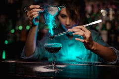 Het vrouwelijke barman gieten op de bruine cocktail en op gevlamde badian op pincet een gepoederde suiker in het groene licht stock afbeelding Het vrouwelijke barman gieten op de bruine cocktail en op gevlamde badian op pincet een gepoederde suiker in het groene licht stock afbeelding