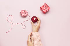Het wijfje dient roze gebreide sweater in houdend een rode Kerstmisbal, legt de giftdoos op roze Vlakte als achtergrond stijl hoo stock afbeelding Het wijfje dient roze gebreide sweater in houdend een rode Kerstmisbal, legt de giftdoos op roze Vlakte als achtergrond stijl hoo stock afbeelding