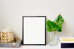 Het zwarte fotokader, de groene installatie in een kristalvaas, de giftvakjes en een stapel van boeken schikten tegen lege grijze royalty-vrije stock afbeelding Het zwarte fotokader, de groene installatie in een kristalvaas, de giftvakjes en een stapel van boeken schikten tegen lege grijze royalty-vrije stock afbeelding