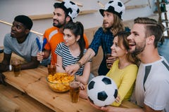 high angle view of smiling multicultural group of friends in soccer ball hats drinking beer and watching football match stock image high angle view of smiling multicultural group of friends in soccer ball hats drinking beer and watching football match stock image