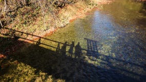 Hikers filming their shadow while crossing over old, wooden bridge over Mirna river at Kamacnik canyon, Croatia