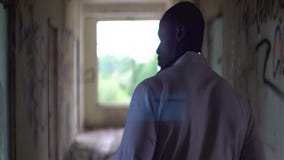 Hintere Ansicht am unbekannten afrikanischen Doktor, der entlang das ruinierte corridord der verlassenen psychiatrischen Klinik g stock footage Hintere Ansicht am unbekannten afrikanischen Doktor, der entlang das ruinierte corridord der verlassenen psychiatrischen Klinik g stock footage
