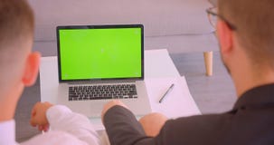 Hinteres Ansichtporträt der Nahaufnahme von zwei erfolgreichen Geschäftsmännern, die zuhause Laptop mit grünem Schirm im Büro ver stock video footage Hinteres Ansichtporträt der Nahaufnahme von zwei erfolgreichen Geschäftsmännern, die zuhause Laptop mit grünem Schirm im Büro ver stock video footage