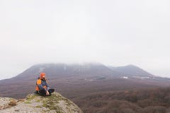 Hipster - a climber in a down jacket and a knitted cap sits and rests on the top of a rock stock images Hipster - a climber in a down jacket and a knitted cap sits and rests on the top of a rock stock images