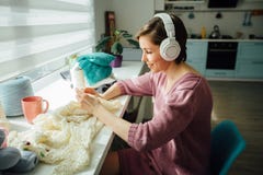 Hobby-, lynne- och fritidbegrepp Kvinna som kopplar av med hörlurar, medan sticka den mjuka klänningen med virkning i solig dag k royaltyfri fotografi Hobby-, lynne- och fritidbegrepp Kvinna som kopplar av med hörlurar, medan sticka den mjuka klänningen med virkning i solig dag k royaltyfri fotografi