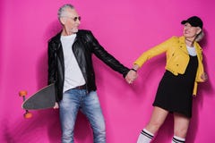 Hoger paar in leerjasjes die met skateboard stellen en handen op roze houden stock foto Hoger paar in leerjasjes die met skateboard stellen en handen op roze houden stock foto