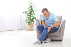 Hogere mens die aan kniepijn lijden in woonkamer stock afbeeldingen Hogere mens die aan kniepijn lijden in woonkamer stock afbeeldingen