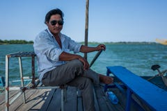 Hoi An, Vietnam - April 21, 2018: Vietnamese captain of local boat steers boat and looks at camera. stock photography Hoi An, Vietnam - April 21, 2018: Vietnamese captain of local boat steers boat and looks at camera. stock photography