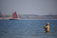 Holnis, Alemania - 8 de abril de 2018 - pescador que se coloca cintura-profundo en el agua de la playa con el velero clásico en e Fotos de archivo Holnis, Alemania - 8 de abril de 2018 - pescador que se coloca cintura-profundo en el agua de la playa con el velero clásico en e Fotos de archivo