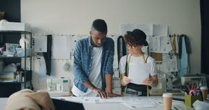Hombre afroamericano de los diseñadores de moda y mujer caucásica que discuten bosquejos almacen de video Hombre afroamericano de los diseñadores de moda y mujer caucásica que discuten bosquejos almacen de video