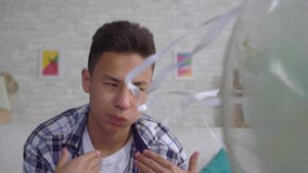 Hombre asiático joven ahorrado del calor que sienta delante de una fan de trabajo el concepto de cierre del calor encima del MES almacen de metraje de vídeo Hombre asiático joven ahorrado del calor que sienta delante de una fan de trabajo el concepto de cierre del calor encima del MES almacen de metraje de vídeo