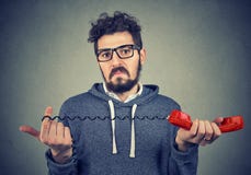 Hombre asqueado que mira la cámara con la confusión que sostiene el microteléfono rojo pasado de moda Foto de archivo Hombre asqueado que mira la cámara con la confusión que sostiene el microteléfono rojo pasado de moda Foto de archivo