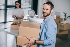 hombre barbudo hermoso que sostiene las cajas de cartón y que sonríe en la cámara mientras que vuelve a poner con el colega femen fotos de archivo hombre barbudo hermoso que sostiene las cajas de cartón y que sonríe en la cámara mientras que vuelve a poner con el colega femen fotos de archivo