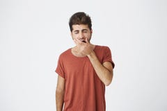 Hombre caucásico hermoso soñoliento que lleva la boca roja de la cubierta de la camiseta mientras que bosteza, después de confere imagen de archivo libre de regalías Hombre caucásico hermoso soñoliento que lleva la boca roja de la cubierta de la camiseta mientras que bosteza, después de confere imagen de archivo libre de regalías