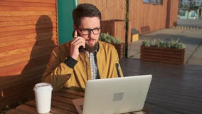 Hombre con hablar al aire libre del ordenador portátil en el teléfono almacen de metraje de vídeo Hombre con hablar al aire libre del ordenador portátil en el teléfono almacen de metraje de vídeo