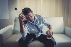 Hombre de negocios alcohólico que lleva el lazo flojo azul bebido con la botella de whisky en el sofá imagen de archivo libre de regalías Hombre de negocios alcohólico que lleva el lazo flojo azul bebido con la botella de whisky en el sofá imagen de archivo libre de regalías