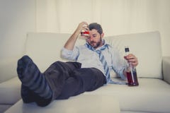 Hombre de negocios alcohólico que lleva el lazo flojo azul bebido con la botella de whisky en el sofá imagen de archivo libre de regalías Hombre de negocios alcohólico que lleva el lazo flojo azul bebido con la botella de whisky en el sofá imagen de archivo libre de regalías