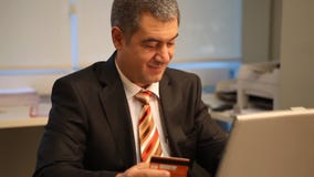 Hombre de negocios con la tarjeta de crédito, usando el ordenador portátil en oficina metrajes Hombre de negocios con la tarjeta de crédito, usando el ordenador portátil en oficina metrajes