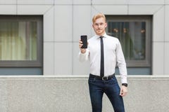 Hombre de negocios del éxito que muestra el nuevo teléfono elegante y que mira la cámara Imagenes de archivo Hombre de negocios del éxito que muestra el nuevo teléfono elegante y que mira la cámara Imagenes de archivo