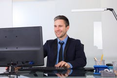 Hombre de negocios feliz usando el ordenador en su oficina foto de archivo libre de regalías Hombre de negocios feliz usando el ordenador en su oficina foto de archivo libre de regalías