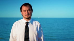 Hombre de negocios joven cerca del mar azul almacen de video Hombre de negocios joven cerca del mar azul almacen de video