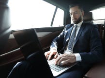 Hombre de negocios que se sienta en el asiento de atrás de un coche, usando su ordenador portátil Foto de archivo Hombre de negocios que se sienta en el asiento de atrás de un coche, usando su ordenador portátil Foto de archivo