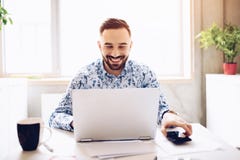 Hombre de negocios sonriente feliz caucásico que trabaja en el ordenador portátil en su oficina foto de archivo libre de regalías Hombre de negocios sonriente feliz caucásico que trabaja en el ordenador portátil en su oficina foto de archivo libre de regalías