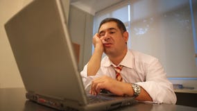Hombre de negocios soñoliento usando el ordenador portátil en oficina almacen de video Hombre de negocios soñoliento usando el ordenador portátil en oficina almacen de video