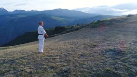 Hombre en karate del entrenamiento del kimono blanco y de la correa negra en fondo de la montaña cámara lenta aérea 4k Hombre en karate del entrenamiento del kimono blanco y de la correa negra en fondo de la montaña cámara lenta aérea 4k