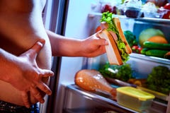 Hombre hambriento que sostiene un bocadillo en sus manos y situación al lado de foto de archivo libre de regalías Hombre hambriento que sostiene un bocadillo en sus manos y situación al lado de foto de archivo libre de regalías