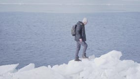Hombre hermoso barbudo rubio joven que lleva la chaqueta, el sombrero caliente y las botas subiendo el glaciar, caminando en el b almacen de metraje de vídeo Hombre hermoso barbudo rubio joven que lleva la chaqueta, el sombrero caliente y las botas subiendo el glaciar, caminando en el b almacen de metraje de vídeo