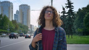 Hombre hermoso Nerdy en vidrios con el pelo rizado que comprueba el teléfono y para el taxi que espera, sosteniendo smartphone di almacen de metraje de vídeo Hombre hermoso Nerdy en vidrios con el pelo rizado que comprueba el teléfono y para el taxi que espera, sosteniendo smartphone di almacen de metraje de vídeo
