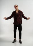 Hombre joven del modelo hermoso en vaqueros y negro negros con la camisa y las gafas de sol rojas en un fondo gris imagen de archivo libre de regalías Hombre joven del modelo hermoso en vaqueros y negro negros con la camisa y las gafas de sol rojas en un fondo gris imagen de archivo libre de regalías