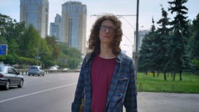 Hombre joven elegante en vidrios con el taxi que espera largo y el tacto del pelo rizado para de su pelo, colocándose en parada d almacen de metraje de vídeo Hombre joven elegante en vidrios con el taxi que espera largo y el tacto del pelo rizado para de su pelo, colocándose en parada d almacen de metraje de vídeo
