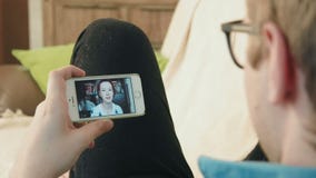Hombre joven que tiene una conversación video de la charla sobre su smartphone con la mujer joven del inconformista Hombre joven que tiene una conversación video de la charla sobre su smartphone con la mujer joven del inconformista