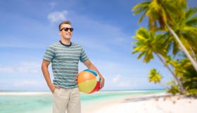 Hombre joven sonriente en gafas de sol con la pelota de playa imagen de archivo libre de regalías Hombre joven sonriente en gafas de sol con la pelota de playa imagen de archivo libre de regalías