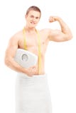Hombre muscular hermoso en la toalla que sostiene una escala del peso foto de archivo Hombre muscular hermoso en la toalla que sostiene una escala del peso foto de archivo