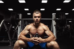 Hombre muscular joven que se sienta con una botella de agua en el gimnasio foto de archivo libre de regalías Hombre muscular joven que se sienta con una botella de agua en el gimnasio foto de archivo libre de regalías